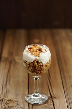 Granola in glass with yogurt on wooden background vertical