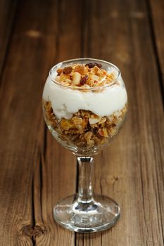 Granola in glass with yogurt on wooden background vertical