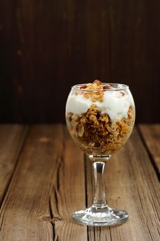 Granola in glass with yogurt on wooden background vertical