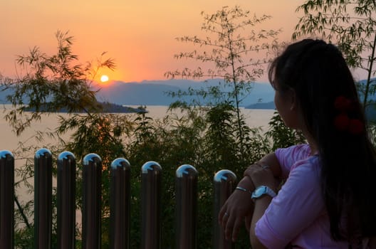 Happy young woman standing on the hill watching the sunset over the lake in Kaeng Kra Chan National Park, Phetchaburi Province, Thailand