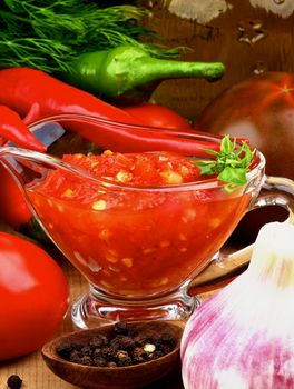 Bruschetta Sauce in Glass Gravy Boat and Black Tomatoes, Garlic, Chili Peppers closeup on Glass Bottle of Olive Oil and Greens background