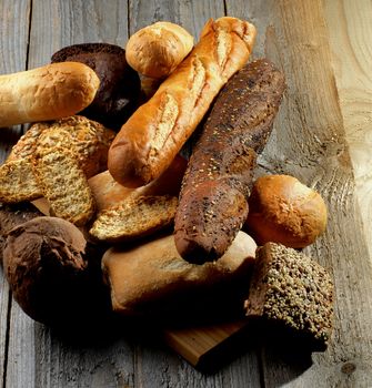 Heap of Various Various Buns, Baguette, Poppy Seed and Sesame Buns, Rye and Whole Wheat Bread isolated on Rustic Hardwood background