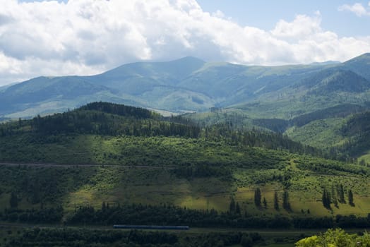 Summer landscape in the Ukrainian Carpathian Mountains with the passenger train passing by.