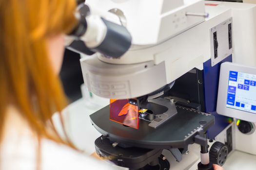 Young female scientist microscoping on hi-tec fluorescent microscope. . Health care professional in hes working environment.