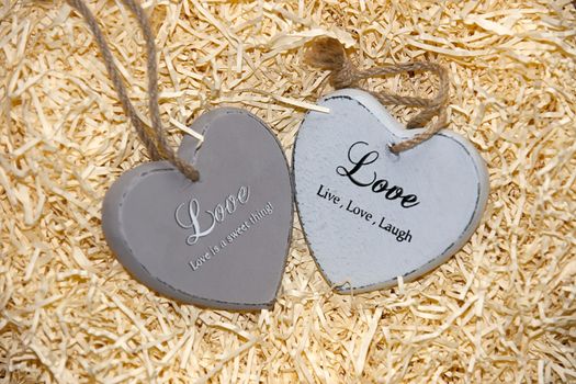 two grey wooden love hearts in a love nest made of straw with loving inscriptions