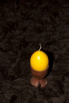 unlit yellow egg shaped candle in an egg cup on a brown carpet