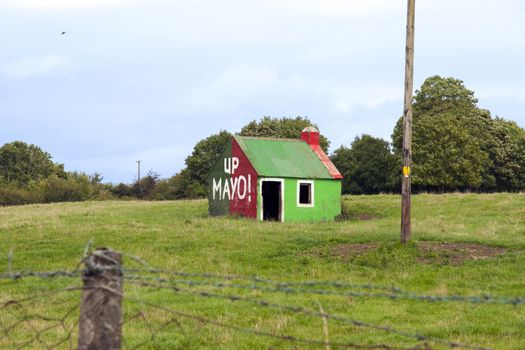 an old shed in a field with the county football colours and up mayo painted on