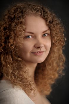 Smiling fairy woman with red curly hair, big breast on dark grey background vertical portrait