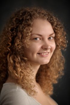 Smiling fairy woman with red curly hair, big breast on dark grey background vertical portrait