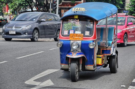 BANGKOK - AUG 23: A three wheeled tuk tuk taxi transports passengers along road, August 23, 2012 in Bangkok, Thailand. Tuk tuks can be hired from as little as $1 or B30 a fare for short trips