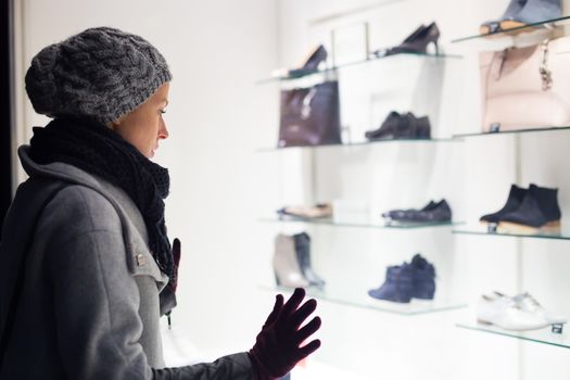 Casualy winter dressed lady window shopping in front of sinfully expensive boutique store dispaly window. Customer woman in shopping street, looking at window, outdoor.