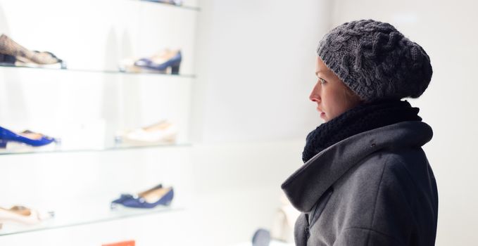 Casualy winter dressed lady window shopping in front of sinfully expensive boutique store dispaly window. Customer woman in shopping street, looking at window, outdoor.