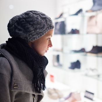 Casualy winter dressed lady window shopping in front of sinfully expensive boutique store dispaly window. Customer woman in shopping street, looking at window, outdoor.