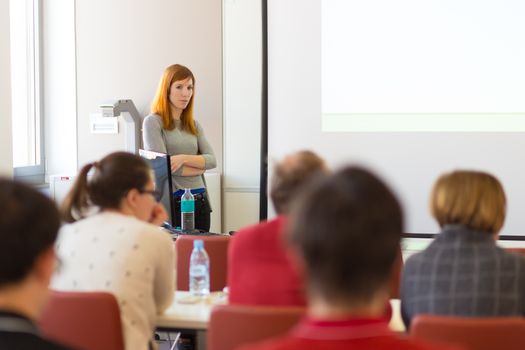 Speaker giving presentation in lecture hall at university. Participants listening to lecture and making notes.