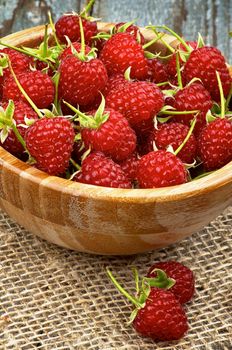 Perfect Ripe Raspberries with Stems in Wooden Bowl closeup on Sackcloth and Rustic Wooden background