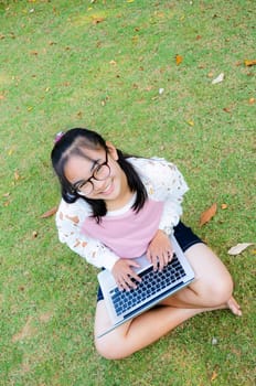 Lovely girl is happy with a laptop on lawn in park