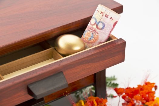 Chinese yuan currency and gold nest egg nestled in wood drawer