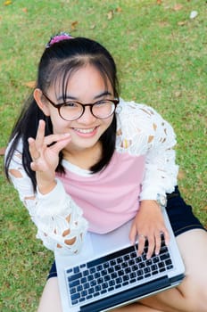 Lovely girl is happy with a laptop on lawn in park