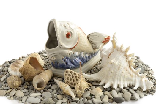 Figure porcelain fish with shells on the sea pebbles.
