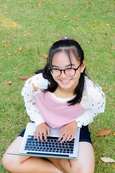 Lovely girl is happy with a laptop on lawn in park