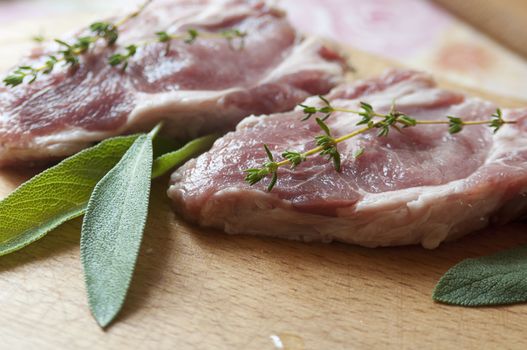 Raw pork steaks with salvia leaves and thyme branches