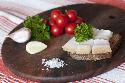 Sandwich made of salted lard on rye bread, served with garlic, cherry tomatoes and parsley