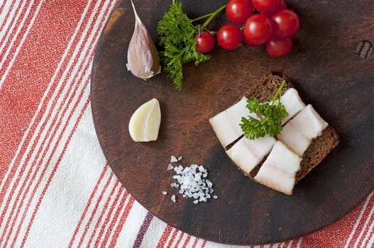 Sandwich made of salted lard on rye bread, served with garlic, cherry tomatoes and parsley