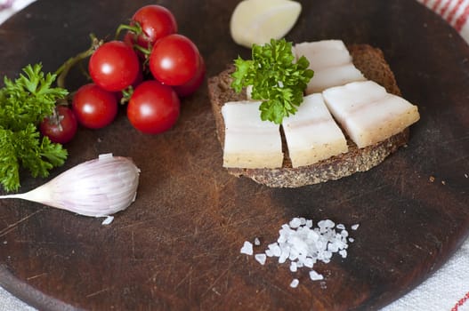 Sandwich made of salted lard on rye bread, served with garlic, cherry tomatoes and parsley