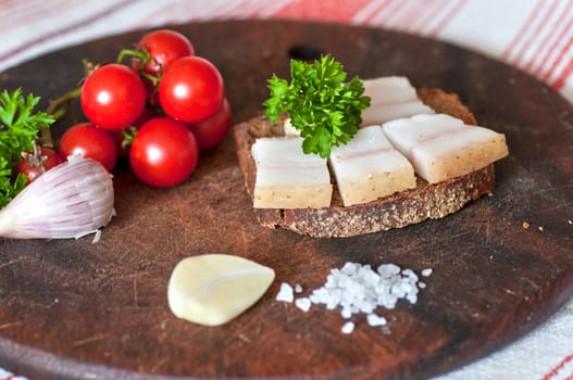 Sandwich made of salted lard on rye bread, served with garlic, cherry tomatoes and parsley