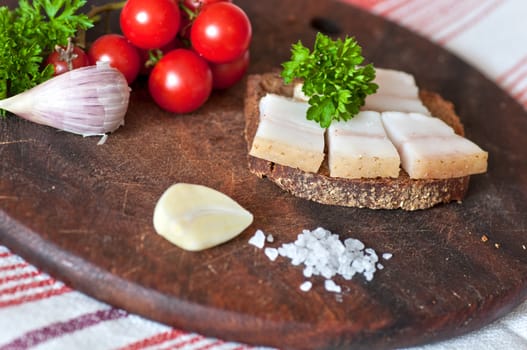 Sandwich made of salted lard on rye bread, served with garlic, cherry tomatoes and parsley