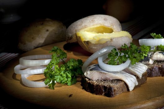 Sandwich made of herring on rye bread, served with onion, jacket potato and parsley