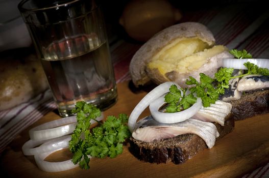 Sandwich with herring on rye bread, served with onion, jacket potato and glass of vodka