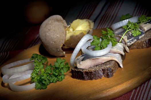 Sandwich made of herring on rye bread, served with onion, jacket potato and parsley