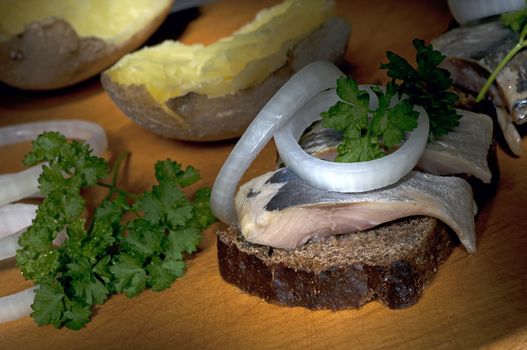 Sandwich made of herring on rye bread, served with onion, jacket potato and parsley