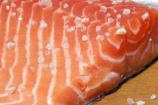 Fresh salmon fillet salted with coarse sea salt close up