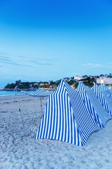 White and blue tents on the beach at sunset.