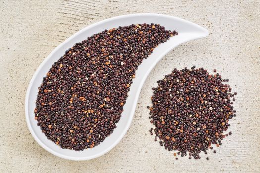 gluten free black quinoa grain grown iin Bolivia ,  a teardrop shaped bowl against white painted grunge wood, top view