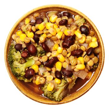 Vegan lentil soup and veggies in bowl with black beans, broccoli, onion, corn over white. Top view.