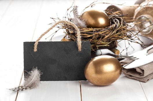 table decoration on white wooden background with chicken golden egg, with blackboard with space for text