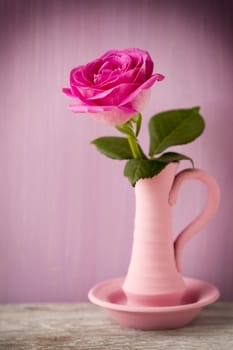 Pink roses in a vase with a Valentine's Day decoration on a wooden shelf.