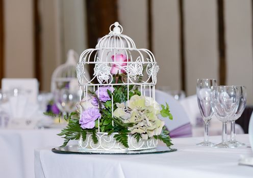 Floral arrangement at wedding reception on table includes lilac flower and glasses