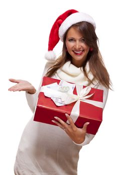 Vivacious beautiful young woman wearing a Santa hat with a large red Christmas gift and money, conceptual of successful Xmas shopping and payment, on white