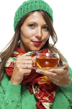 Attractive young woman in a trendy green knitted winter ensemble warming up with a cup of hot tea isolated on white