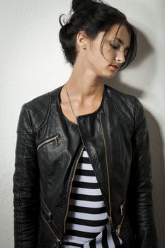 Pretty Young Woman in Black Leather Jacket Holding her Black Hair While Facing Right. Captured with Gray Wall Background.