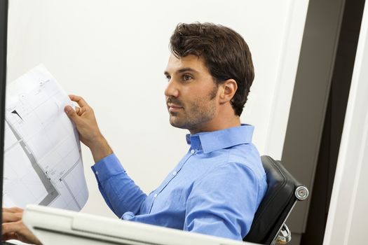 Young handsome man sitting at his desk in the office while reading written agreements and studying important documentation for work