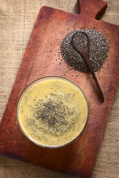 Overhead shot of mango pudding with chia seeds (lat. Salvia hispanica) on wooden board photographed with natural light. Chia seeds are considered a superfood containing proteins, omega fats, minerals and antioxidants. (Selective Focus, Focus on the top of the pudding)