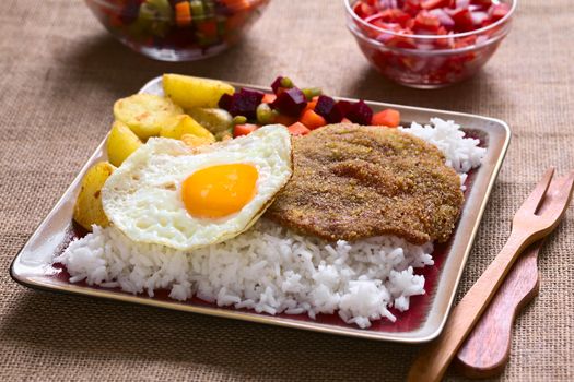 Traditional Bolivian dish called Silpancho, which is the name of the breaded flat, round piece of beef meat, served with fried egg, rice, fried potatoes and vegetables (carrot, bean, beetroot), photographed with natural light (Selective Focus, Focus one third into the dish)