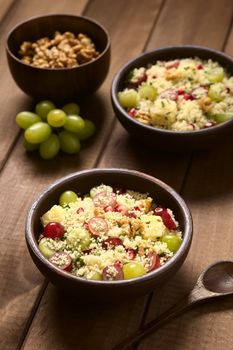 Two bowls of vegetarian couscous salad with grapes, pomegranate, walnuts, cheese, lime and mint, photographed with natural light (Selective Focus, Focus in the middle of the first salad)