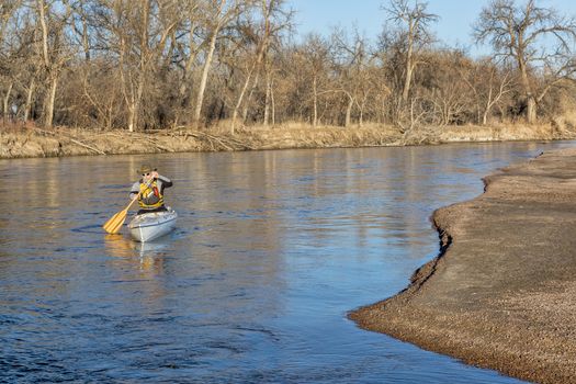 senior paddler in a decked expedition canoe on the South Platte River in eastern Colorado, winter scenery without snow