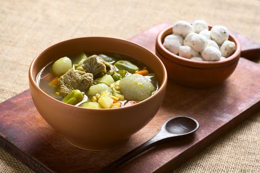 Bolivian traditional soup called Chairo de Tunta (tunta is a freeze-dried potato typical in the Andean regions) made of tunta, beef, broad beans, peas and carrots, uncooked tunta in the back, photographed with natural light (Selective Focus, Focus one third into the soup)    